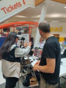 Komal is looking through VR glasses attached to a stand. Julian is watching