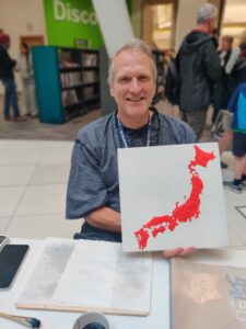 Andy, holding up a 3d printed map of Japan, in red on a white background